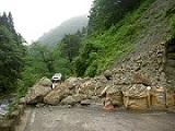 山道で土砂崩れが起きていて、岩の上に車が停まっている写真
