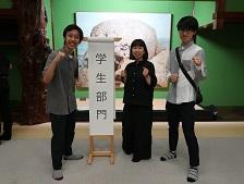 金澤町家学生会議 情報発信班の関係者3人が「学生部門」と書かれた紙のめくり台に立っている画像
