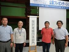 夕日寺1300年協議会の関係者4人が「採択実績団体部門」と書かれためくり台の横に立っている画像