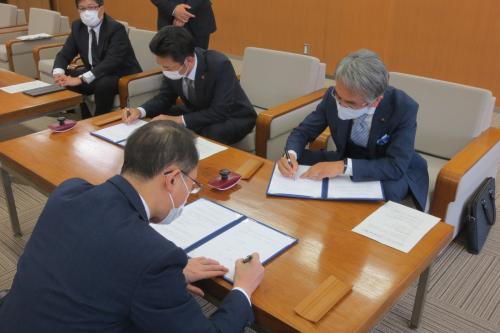 机上で協定書にサインをする3名の男性の写真