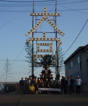 丸太で大宮と造られたご神門の前で地域の関係者の人達が集まって記念撮影をしている写真