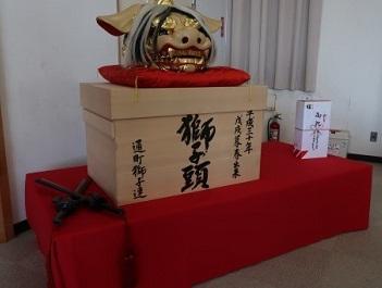 「獅子頭」と書かれた箱の上に金色の獅子の頭が飾られている写真