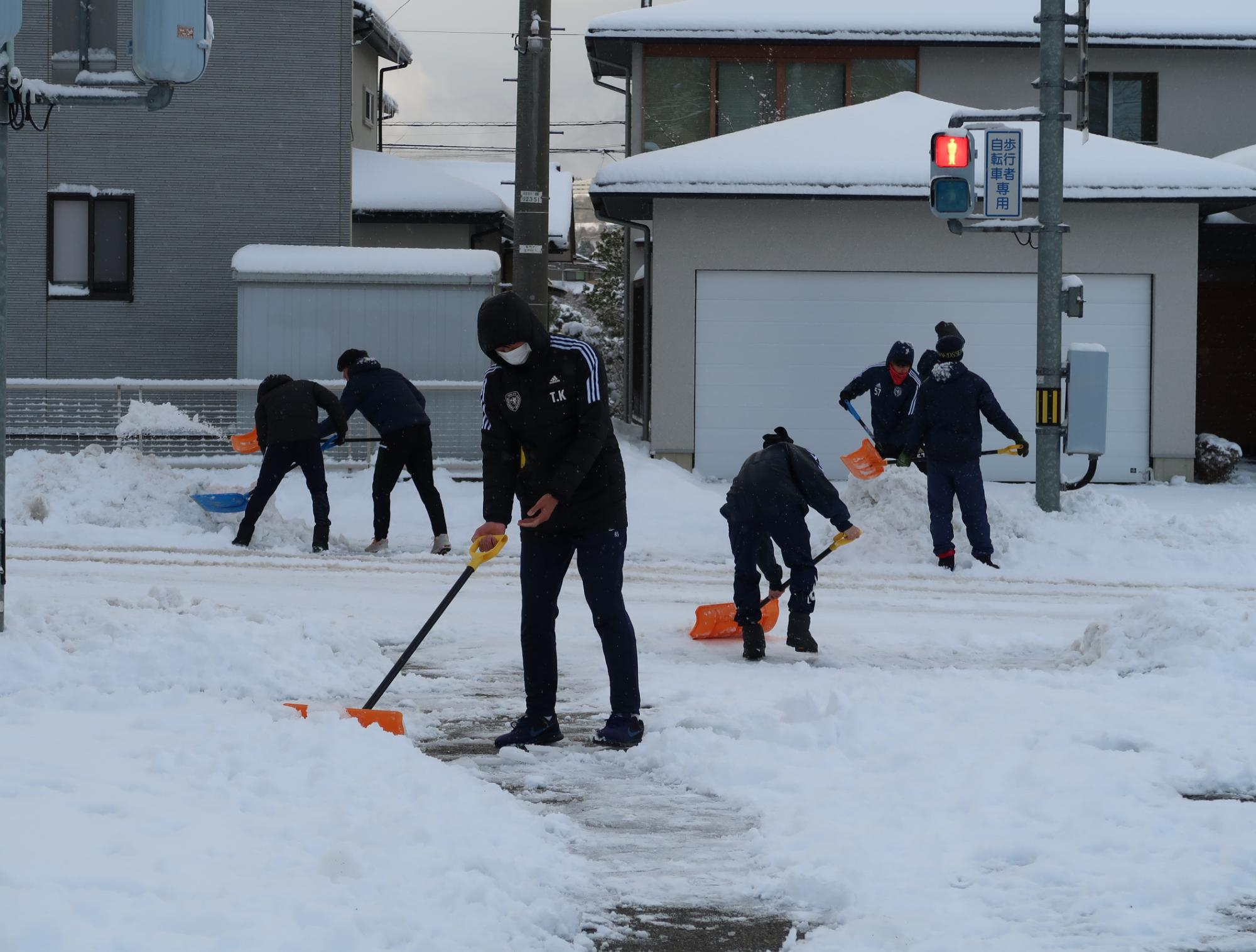 ボランティアの方が道路に積もった雪をスコップを手に雪かきをしている写真