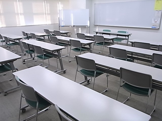 テーブルと椅子が並び、室内前方に脚付きのホワイトボードと壁にホワイトボードが掛かっている研修室の写真
