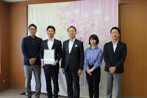 桜の絵の前で石川県人材事業協議会の関係者4名と市長が並んでいる写真