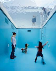プールの中にいるような部屋で大人や子供たちが揺れる天井の水面を眺める写真