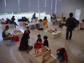 木造の積み木などのおもちゃが乗っている台が各地に設置されているキッズスタジオの写真