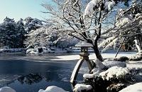 凍った池をバックに、周囲の木々や灯篭に雪が積もっている銀世界の兼六園の写真