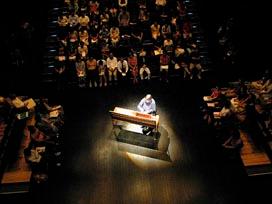 ホールlの中央でピアノを弾く男性を左右後ろの3方から囲む座席で観客が眺める写真