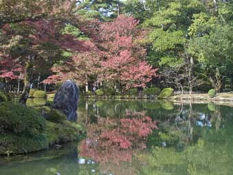 池の畔に立つ樹木の葉が、紅く色づき始めた霞ヶ池畔の写真