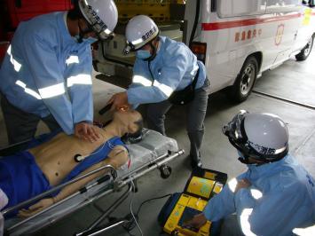 ストレッチャーに横たえた訓練用人形に心臓マッサージをする隊員、AEDの操作タイミングを見計らっている隊員、気道確保をしている隊員の写真