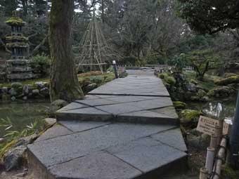 池に架かる、斜めに筋が入った模様の石で造られた日暮らしの橋の写真