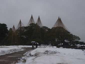 雪が降る中、奥の唐崎松へ向かって続く通路を、2名の観光客が傘をさして歩いている写真