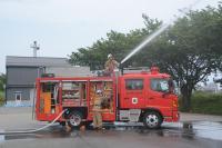 消火ホースを使う訓練の様子を撮影した写真。消防車の上に消防士が乗り放水をしている。