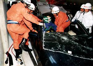 事故に遭った黒い乗用車からドライバーを救出する消防隊員の写真