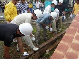 白いヘルメットをかぶった男性たちが長い木材をのこぎりで切断している写真