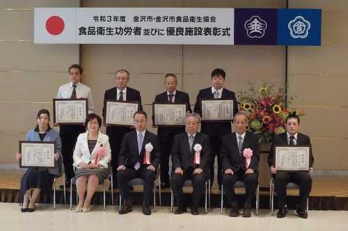 中央に市長、横と後ろに表彰状をもった表彰者たちや胸に花をつけた関係者達が10名が並んでいる記念写真
