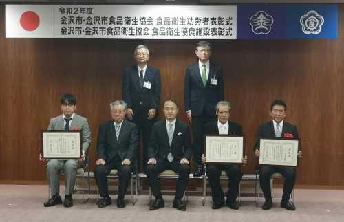 中央に市長、両脇に表彰者、後ろに関係者2名の計7名が並んでいる記念写真