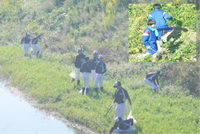 川辺で野球着姿やジャージ姿の生徒たちがゴミ拾いをしている写真
