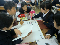生徒たちが集まり机の上に置かれたホワイトボードに文字を書いている写真