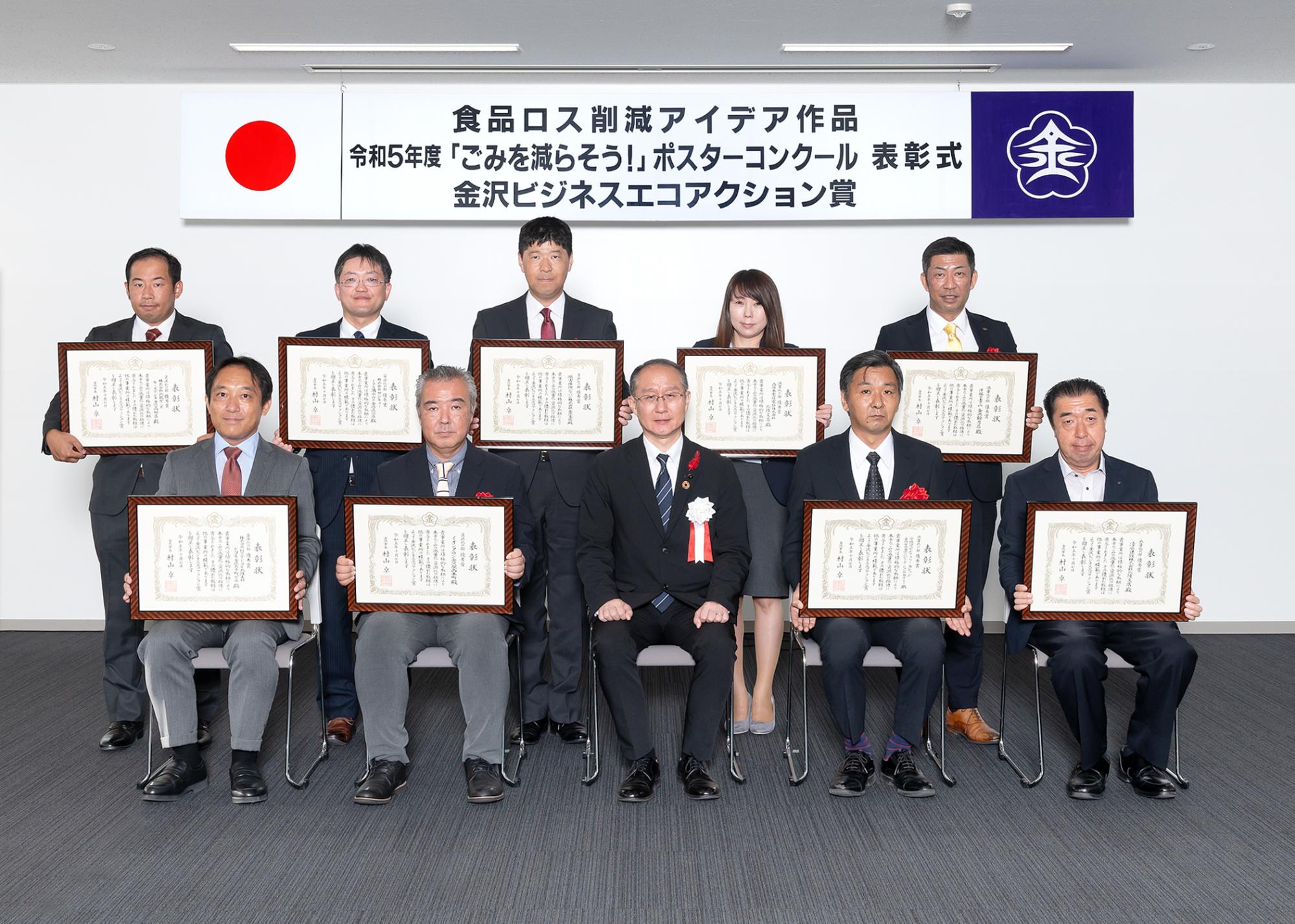 「令和3年度金沢ビジネスエコアクション賞表彰式」と書かれた横断幕の前で、額に入った賞状を持った受賞者10名と市長が記念撮影をしている写真