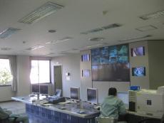 壁の沢山のモニター画面に映像が映し出されている中央監視室の写真