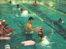 男性の指導を受けながら子ども達がプールで泳ぎの練習をしている写真