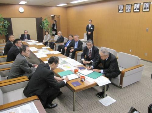 市長応接室で中央に置かれたテーブルの左側に4名の男性、右側に5名の男性と1人の女性が座っており、手間に座っている市長と関係者の男性が書類に記入をしている写真