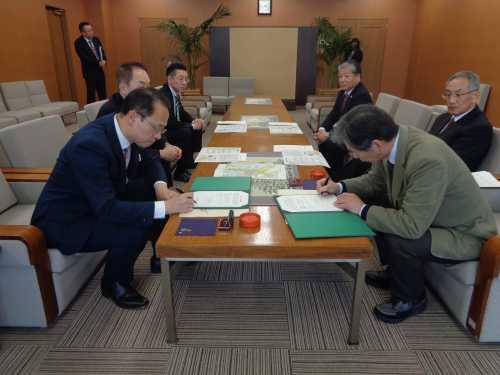 テーブルの端に座っている市長と新影会の関係者の男性がそれぞれの書類に記入をしている写真
