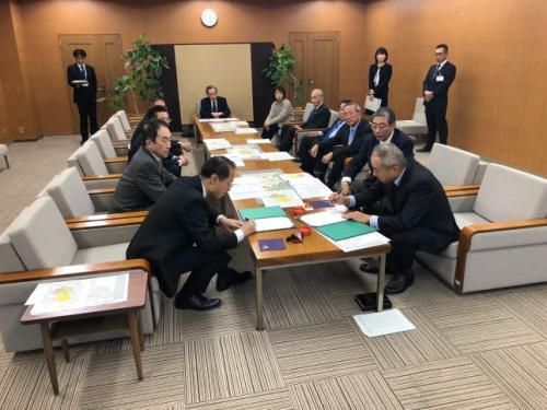 参加している関係者達が見守る中、テーブルの手前側に座っている山野金沢市長と関係者の男性がそれぞれの書類に記入をしている写真