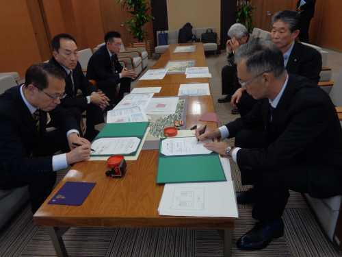 手前に座っている市長と五宝町下組町会の関係者の男性がそれぞれの協定書に記入をしている写真