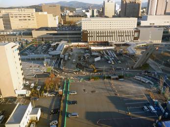 平成24年12月の工事進捗、北西から撮影した写真。手前の駐車場の左側に緑の柵が立てられている。