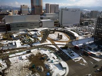 平成25年2月の工事進捗、北西から撮影した写真。一面が雪で覆われていて、駐車場、バスロータリーが写っている。