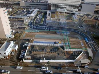 平成25年12月の工事進捗、北西から撮影した写真。手前の駐車場が白い仕切りの中に鉄の棒が等間隔で立てられている。