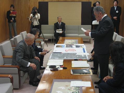 山出金沢市長左側に山出金沢市長と男性1名が座り、向かい側に書類を持った男性が立っており、協定に向けて話し合いが行われている写真