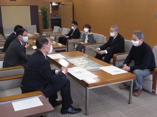 中央にあるテーブルを挟んで左側に男性3人、右側に男性3名と女性1人が椅子に座り話し合いが行われている様子の写真