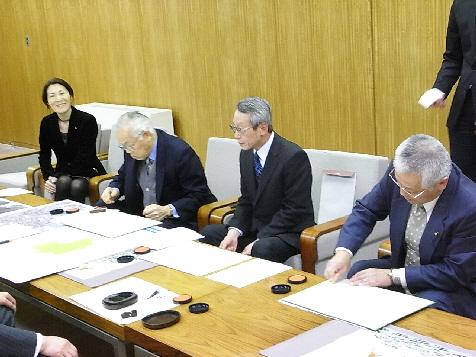 左から笑顔で座っている女性、書類を見ている2人の男性、書類に判を押している男性の写真