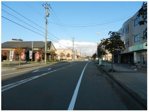 右側にビルのような建物、左側に瓦屋根のある建物、中央に白線が引かれた道路が写っている松村中央病院線の写真