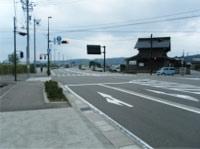 左側に歩道があり少し先に信号機が設置された交差点がある道路の写真