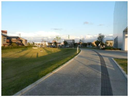右側にアスファルトの通路、左側に芝生の広場が写っている金沢西部図書館（仮称）広場の写真