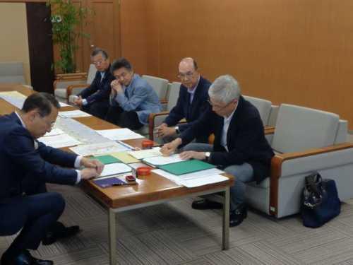 テーブルを挟んで左側の市長と右側の男性がそれぞれの書類に判を付いている写真