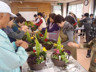 様々な花が鉢に寄せ植えされ、参加者が仕上げをしている写真