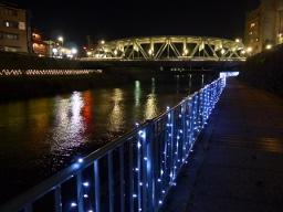 川の柵に飾られた青色のイルミネーションの光が灯っている写真