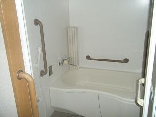 シャワーの近くと、浴槽の上に茶色い手すりがついている浴室の写真