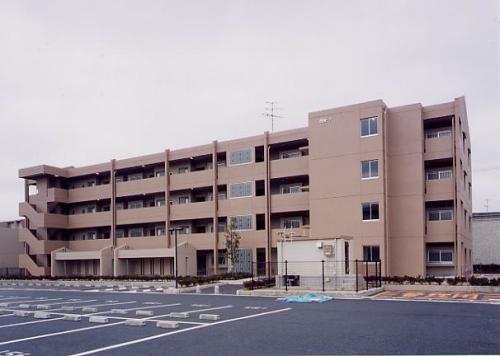 茶色の外壁で4階建ての松寺町住宅の建物と広々とした駐車場の写真