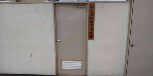 「金沢市降雪作業本部」と書かれた木製の看板が扉の右側の壁に設置されている写真
