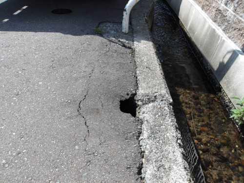 側溝横の道路に穴が空いており、破損している道路補修前の写真