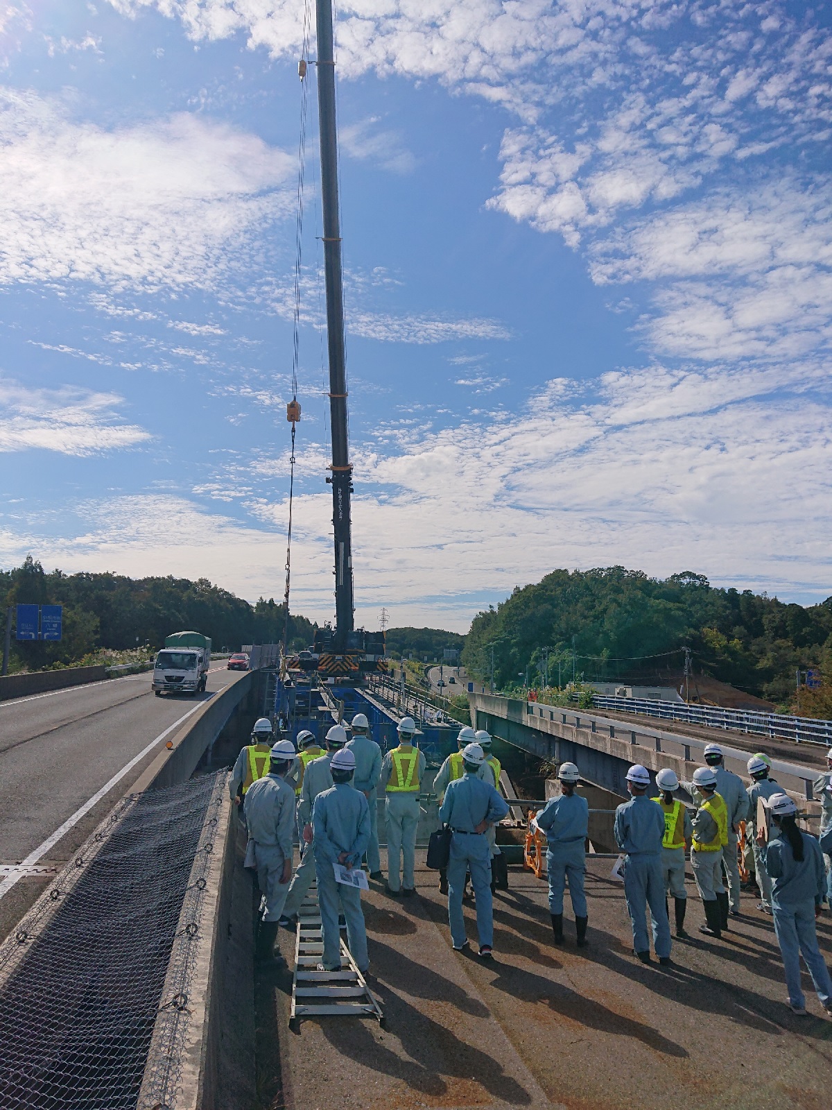 国道8号小松バイパスの橋梁工事の様子。写真中央奥に大型クレーンが作業中。中央手前で見学者たちが工事の様子を見守っている。