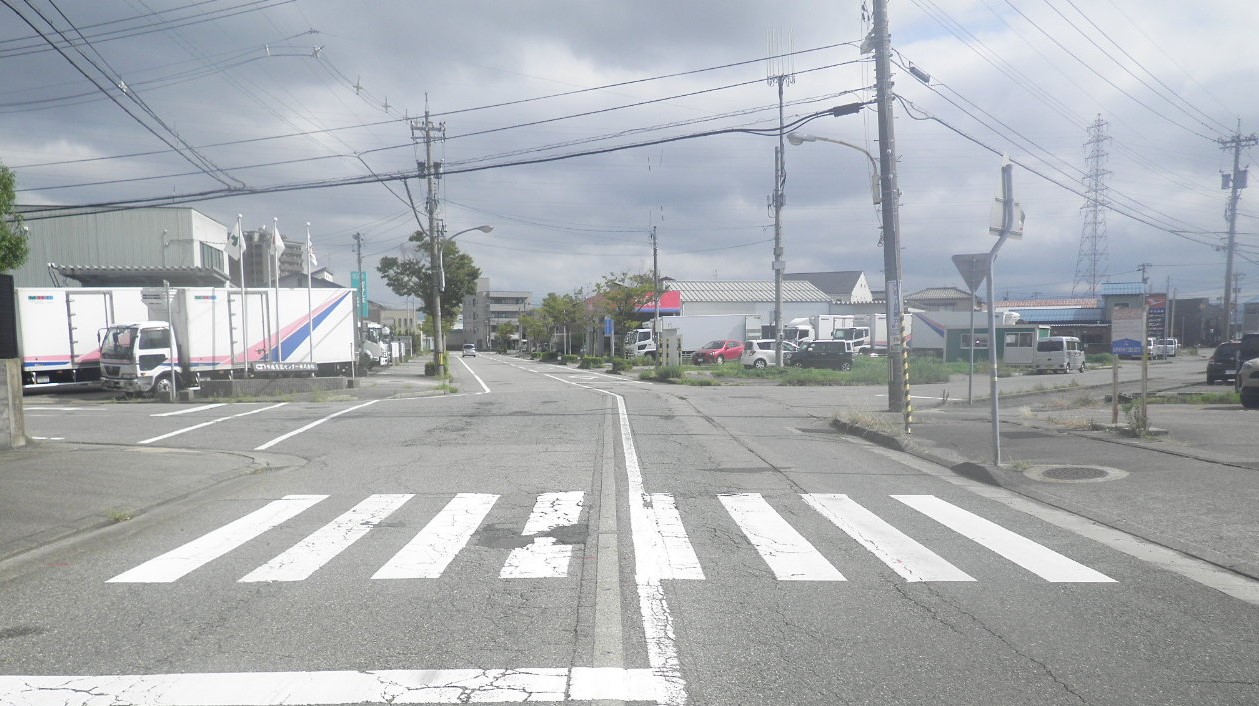補修前。十字路交差点。道路に多数の罅と、手前の横断歩道中央に剥離あり。路側帯の線が消えているところもある。