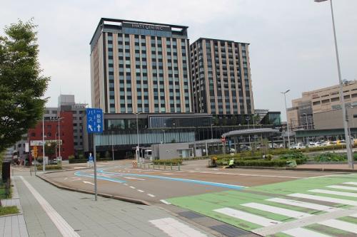 手前の道路に緑色に引かれた横断歩道があり、奥にクロスゲート金沢の建物が写る写真